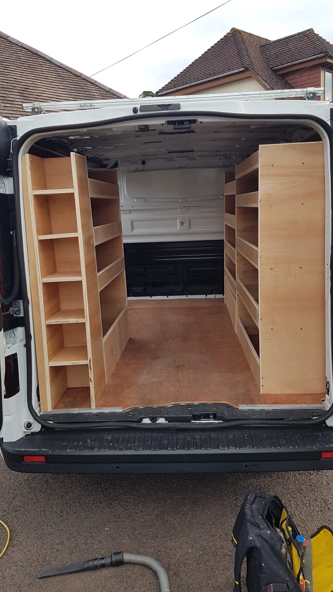 Plywood shelving fitted along both sides of a van, seen from the rear doors